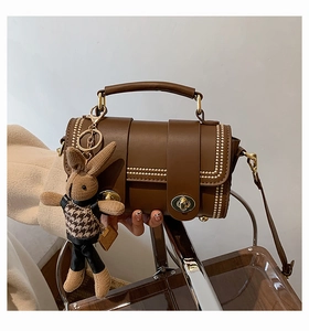 Close-up of retro brown handbag with gold studs, locks and a knit rabbit charm