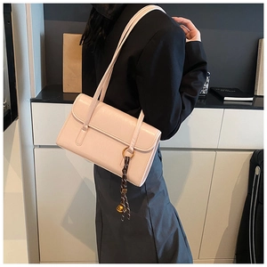 Detail of light pink faux leather shoulder bag with decorative woven charm and dual straps