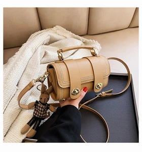 Detail of a khaki cylinder handbag with beaded edges and a plush bunny charm on a sofa
