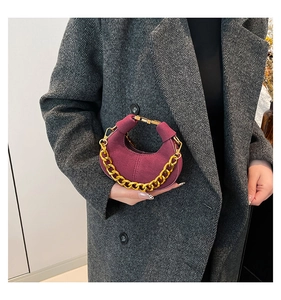 Detalle de bolso medialuna de ante burdeos con cadena dorada sobre un abrigo gris