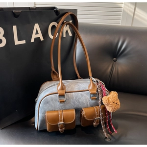 Detail of blue denim Boston bag with brown leather trim and cute plush bear charm
