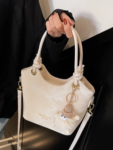 Sac seau chic crème avec poignée nouée et pendentif poupée sur fond minimaliste noir