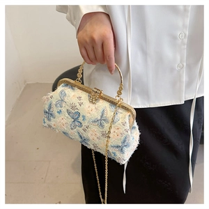 Detail einer hellblauen Sticktasche mit Schmetterlingsmuster und goldenem Rundgriff