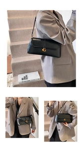 Detail of sleek black leather underarm bag featuring a metallic gold G clasp and strap