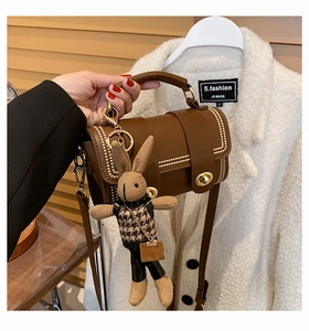 Detail of a brown leather handbag featuring gold rivets and a trendy rabbit charm