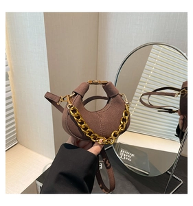 Detalle de bolso medialuna de ante marrón con cadena dorada y correa, visto en un espejo