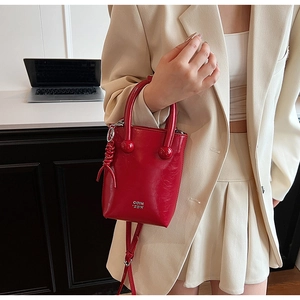 Detail of red wax leather mini handbag with top handles and logo on beige suit background