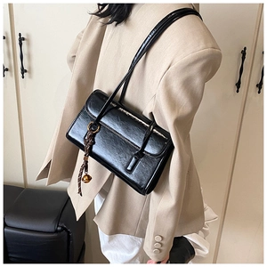 Detail of black glossy shoulder bag featuring brown woven cord and a gold bell pendant