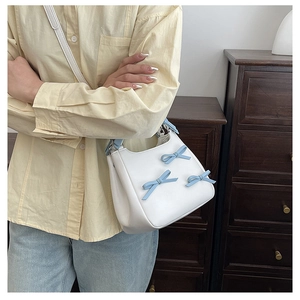 Detail of white leather shoulder bag with three light blue bows on a soft texture surface