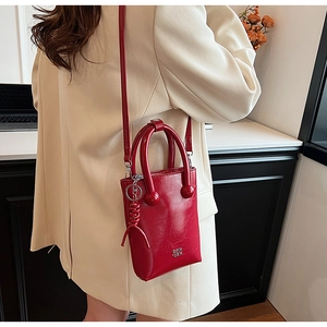 Detail of red wax leather mini handbag with round handles and logo on beige coat
