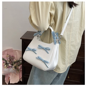Detail of white PU leather bag with blue bows and detachable shoulder strap in lifestyle setting