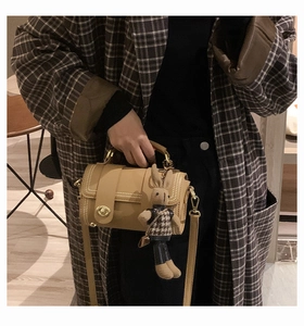 Detail of khaki barrel bag with white stitching, metal clasp and plush rabbit charm