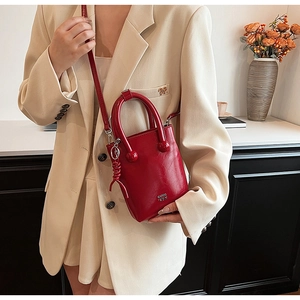 Detail of red oil wax leather crossbody bag with sphere buckle and woven charm decoration