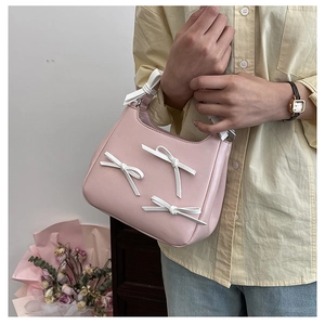 Close-up of pink handheld bag with white bows showing texture and model hand carry