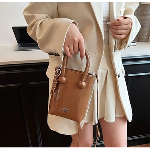 Detail of caramel oil wax leather bag featuring metal ball accents and woven tassel charm