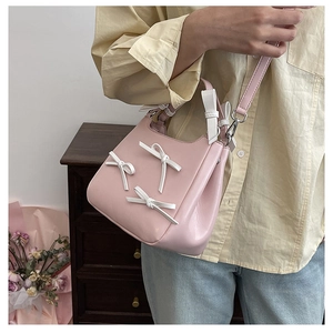 Pink crossbody bag featuring white 3D bow details worn by a model in a cozy home setting