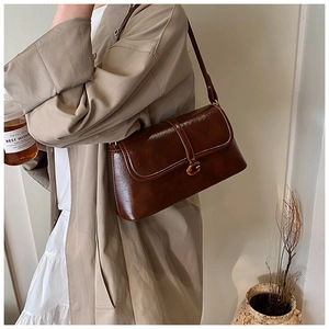 Detail of dark brown glossy underarm bag with golden G-buckle worn on trench coat