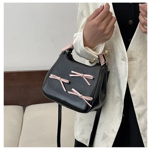 Detail of pink bows on black glossy leather handbag with crossbody strap