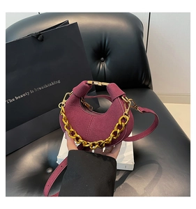 Detalle de bolso medialuna en ante granate con cadena dorada y correa de hombro