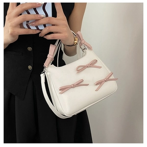 Detail shot of white trapezoid bag featuring three 3D pink bows and top handle