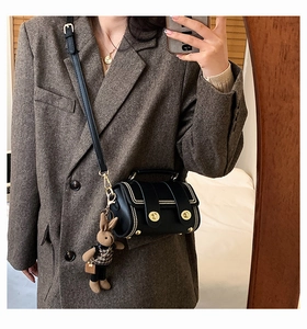 Detail view of a black barrel crossbody bag with gold studs and a cute rabbit charm
