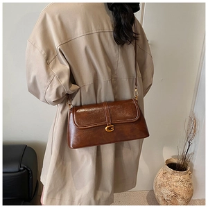 Detail of vintage brown leather bag with gold G-logo and slim strap on beige coat