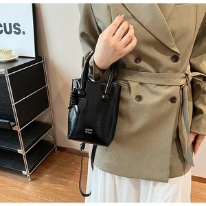 Detail of black glossy leather crossbody bag with braided pendant and white logo text