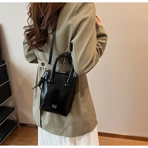 Close-up of black waxed leather bucket bag with silver logo and spiral charm pendant
