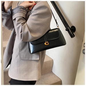 Detail of glossy black leather shoulder bag featuring a prominent gold G-shaped metal buckle