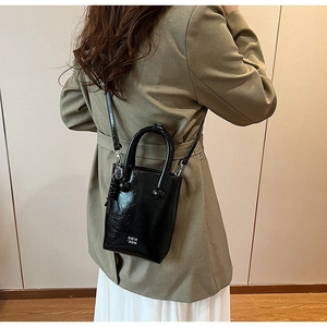Detail view of black glossy mini tote bag with COIN 2DN lettering on a green suit outfit