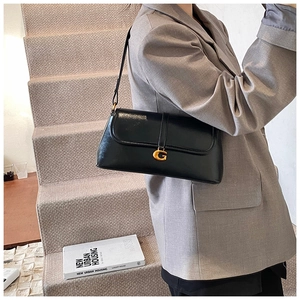 Detail of black glossy shoulder bag with gold G buckle styled with a gray suit blazer