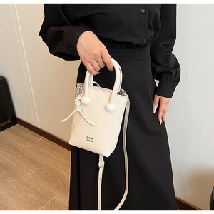 Close-up of cream mini bucket bag with bead details and braided charm on black outfit