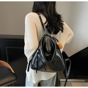 Detailed view of black patent leather tote bag with white contrast stitching and plush charm