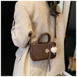 Dettaglio di una borsa a mano marrone in pelle cerata con ciondoli e tracolla regolabile