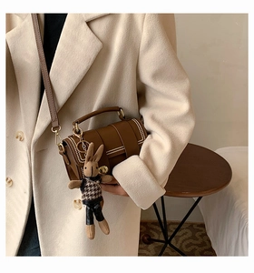 Detail of a brown leather crossbody bag with metal rivets and a cute rabbit charm
