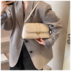 Detail view of a beige underarm bag with golden G buckle shown on a grey suit model