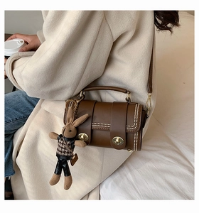 Detail of a brown leather shoulder bag with gold metal rivets and a cute bunny pendant