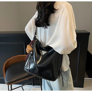 Detail of glossy black tote bag featuring a silver triangle plaque and brown teddy charm