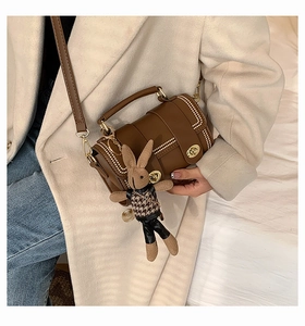 Detail of a brown cylinder bag with white stitching and a cute bunny plush charm
