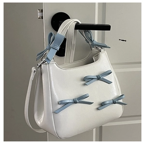 Detailed shot of white faux leather bag featuring light blue bow accents and silver hardware