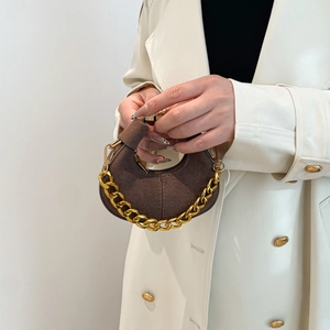 Brown suede crescent handbag with thick gold chain worn by a model in a white coat