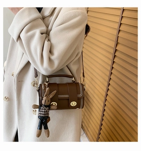 Detail of a brown leather crossbody bag with white beads and a cute rabbit doll charm