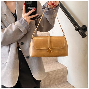 Detail of camel underarm bag with gold G-lock worn by a model in a gray suit