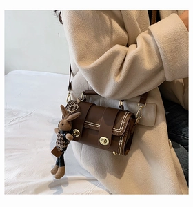 Detail of dark brown cylindrical crossbody bag with gold hardware and rabbit charm