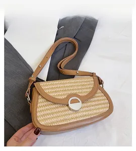 Detailed view of hand-woven straw saddle bag with brown leather trim and silver metal buckle
