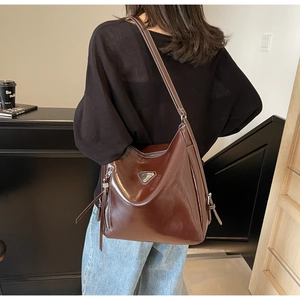 Detail of dark brown leather tote bag with side fringe tassel and metallic triangle logo