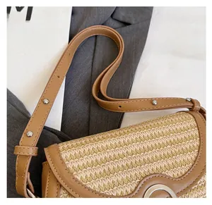 Detail of woven straw bag with brown leather trim and silver metal rivets on shoulder strap
