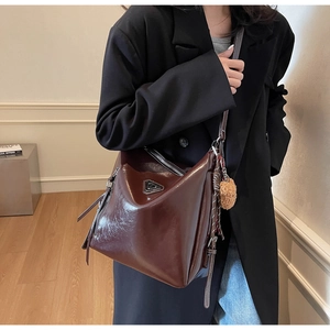Detail view of burgundy tote bag with metal triangle logo and plush ball accessory