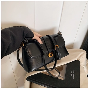 Close-up of elegant black underarm bag with gold G-shaped metal buckle and smooth finish
