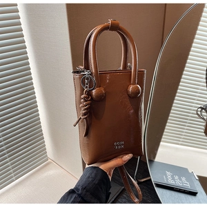 Detail of a brown oil-wax leather handbag featuring a round handle buckle and knot charm